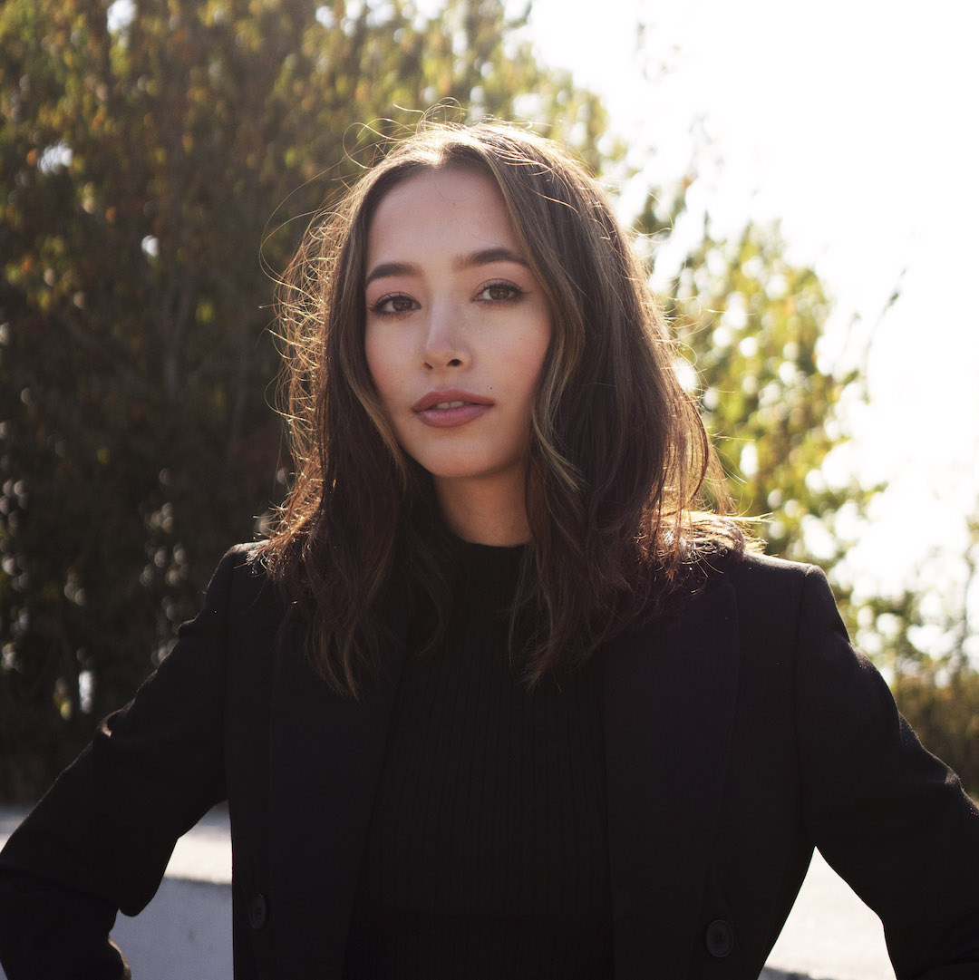 Andini Makosinski headshot. She's posing with her hands on hips, with a soft smile and wearing a black blazer in front of an outdoor backdrop.