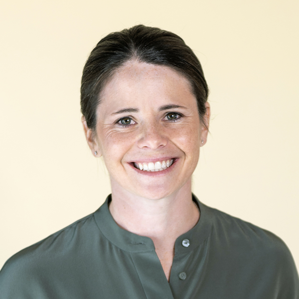 Headshot of Diana Matheson smiling and standing in front of a pale-yellow background and wearing a green button-up blouse.