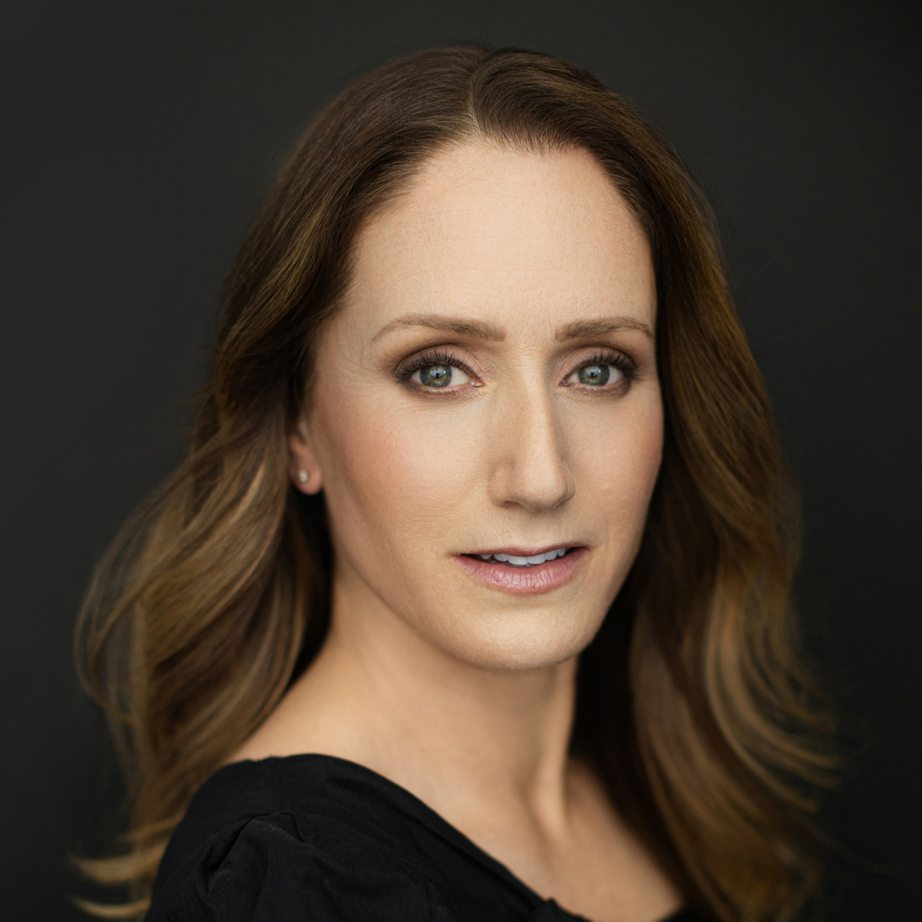 Meghan Gardiner. Headshot or Meghan Gardiner wearing a black top and posing in front of a dark grey background.