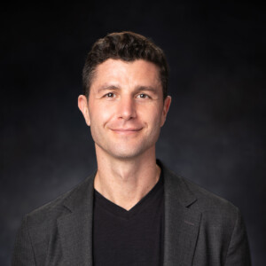 Ben Nemtin. Headshot of Ben Nemtin wearing a dark grey jacket over a black shirt. He is standing in front of a dark grey background.