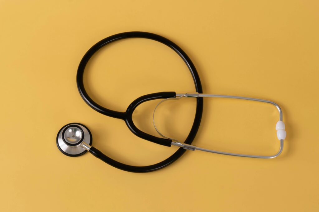 A black and silver stethoscope resting on a solid yellow surface.