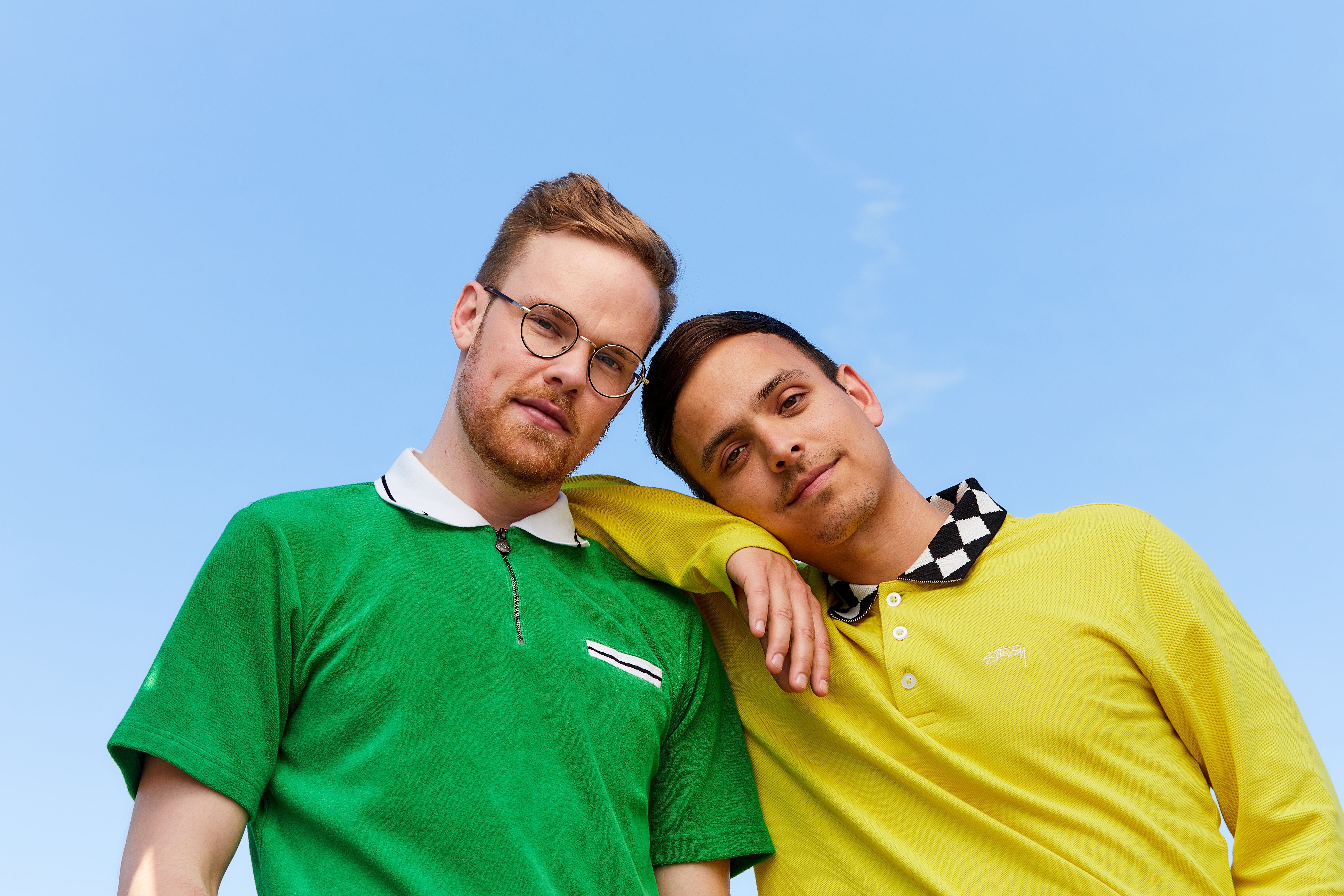 Who is AsapSCIENCE? Headshot of Mitchell Moffit with Gregory Brown. They are standing in front of the blue sky. Mitchell is wearing a yellow long sleeve shirt and is resting his arm and head on the shoulder of Gregory. Gregory is wearing a bright green shirt.