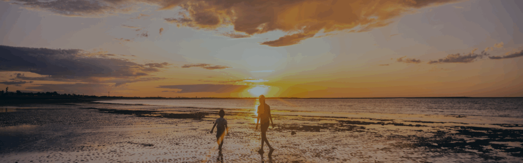 Two people walking on the beach as the sun sets in the background.