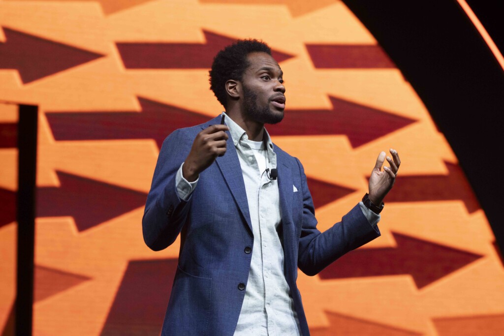 Keynote speaker, Anthony Morgan, speaking on stage at a conference. He is wearing a blue suit jacket.